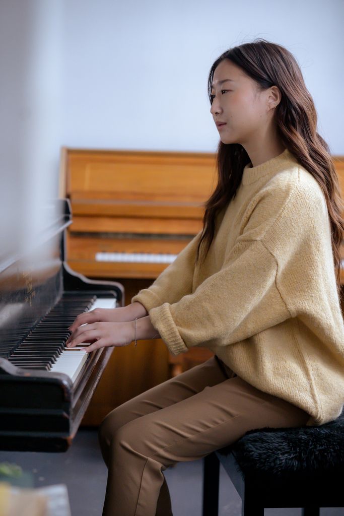 Side view of ethnic woman in casual clothes practicing music on piano while sitting on pouf in bright room